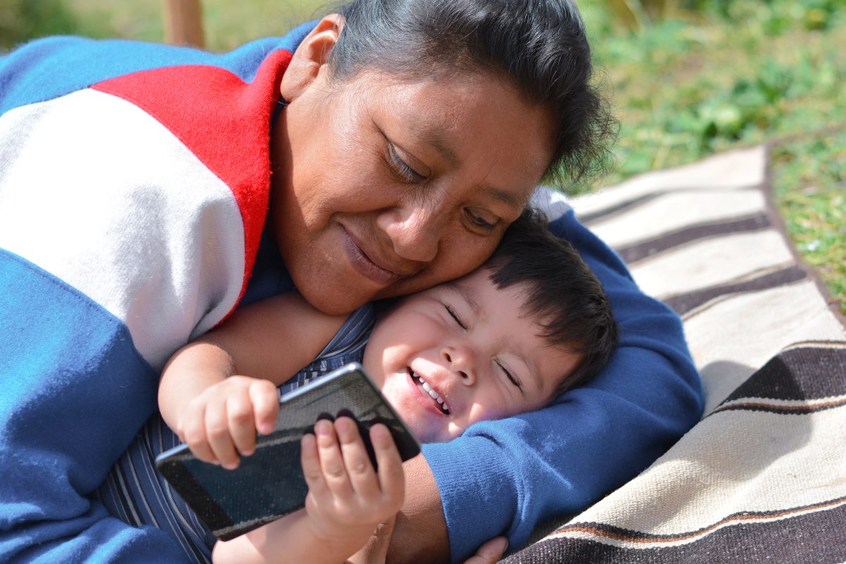 Woman hugging small child holding cell phone.