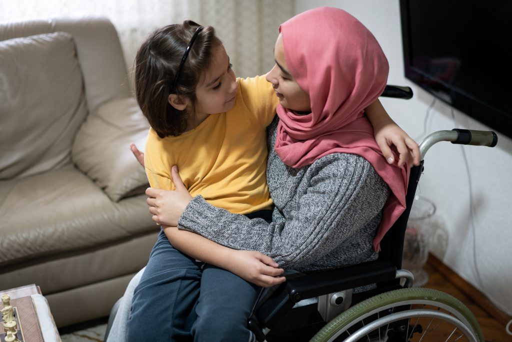 woman wearing hijab in wheelchair with young girl on her lap